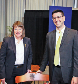 The Brandeis provost and a male professor stand with their hands on the back of a chair